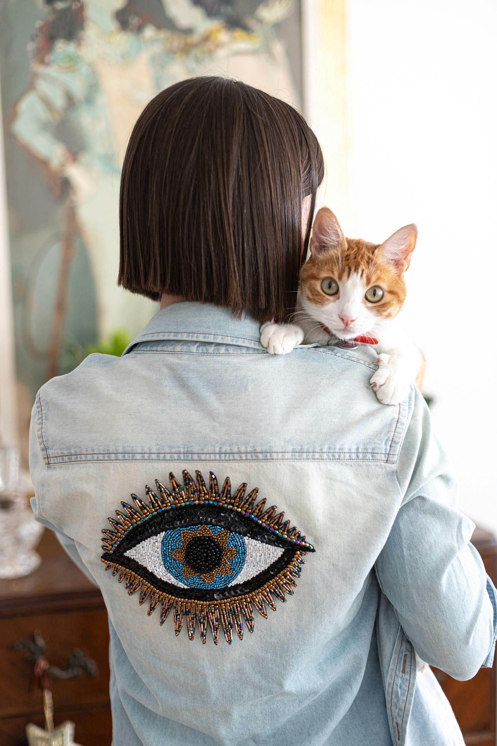 Femme de dos portant une veste customisée avec un oeil. Un chat est perché sur son épaule.