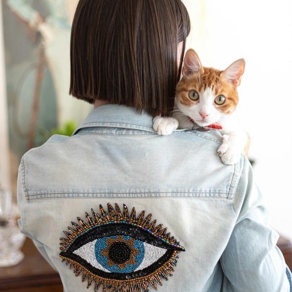 Femme de dos portant une veste customisée avec un oeil. Un chat est perché sur son épaule.